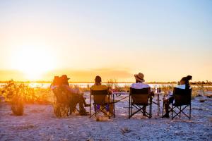 een groep mensen die in stoelen zitten te kijken naar de zonsondergang bij Chobe River Campsite in Ngoma