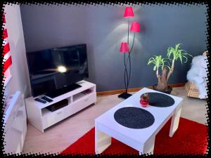 a living room with a tv and two white tables at Résidence des lentilles in Schiltigheim