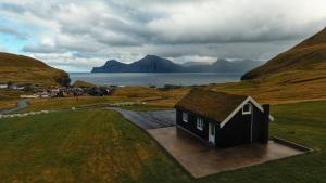 a small house in a field next to a body of water at Iconic Turf-Roof House in Gjógv in Við Gjógv
