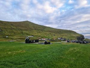 a green field with a small building in front of a hill at Three bedroom vacation home in Við Gjógv