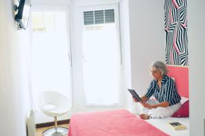 a woman sitting on a bed reading a book at Balenax Pensión in Gijón