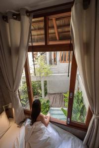 a woman laying on a bed looking out a window at Hidden Garden Hostel in Chiang Mai