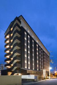 Hotel Route-Inn Sakurai Ekimae في Sakurai: مبنى أسود كبير مع أضواء تعمل