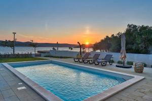 ein Pool mit Stühlen und ein Sonnenuntergang im Hintergrund in der Unterkunft Villa Roberta in Turanj