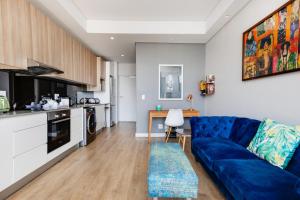 Una sala de estar con un sofá azul y una cocina. en Backup-Power Eclectic Blue City View Apartment, en Ciudad del Cabo