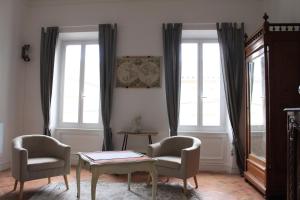 sala de estar con 2 sillas, mesa y 2 ventanas en CHIC ANDREOSSY-COSY-AUTHENTIQUE-WI-Fi-Vélo, en Castelnaudary