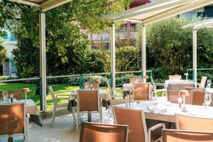 un restaurante con mesas blancas, sillas y árboles en Hotel Savoy en Grado