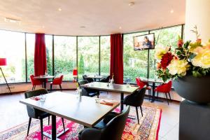 een restaurant met tafels en stoelen en grote ramen bij Bastion Hotel Roosendaal in Roosendaal