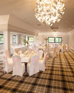 um quarto com mesas e cadeiras brancas e um lustre em Crowwood Hotel and Alba Restaurant em Chryston