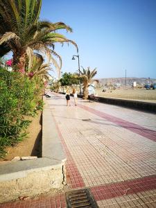two people walking down a street with palm trees at PLAYA LAS VISTAS LOFT in Los Cristianos