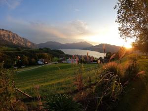 a sunset over a field with a lake and mountains at Biohof Schwanser in Steinbach am Attersee