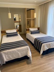 una camera d'albergo con due letti con cuscini a righe di Astron Suítes São José dos Pinhais by Nobile a São José dos Pinhais
