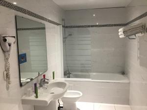 a white bathroom with a tub and a sink and a toilet at Hôtel Angelic in Lourdes