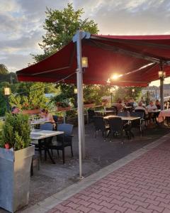 Un groupe de personnes assises à des tables sous un parapluie rouge dans l'établissement Pension Da Enzo, à Otterbach