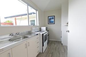 a kitchen with white cabinets and a sink and a window at Aden Motel in Te Anau