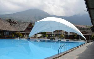 une grande piscine bleue avec un parasol blanc dans l'établissement Kampung Sumber Alam Garut, à Garut