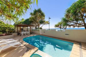 una piscina con sedie, tavolo e alberi di Portofino 1 - Beachfront Apartment Noosa Heads a Noosa Heads