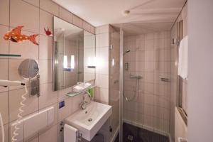 een badkamer met een wastafel, een douche en een spiegel bij Hotel Maximilians in Essen