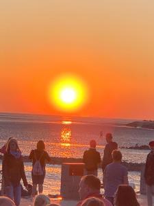 - un groupe de personnes debout sur la plage pour admirer le coucher du soleil dans l'établissement Austernfischer, à Büsum