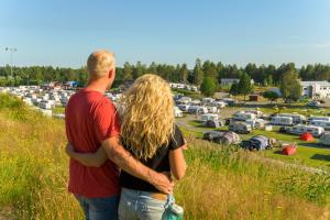 un hombre y una mujer de pie en un campo mirando un estacionamiento en Skellefteå Camping, en Skellefteå