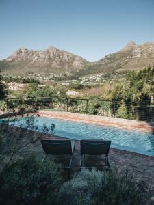a pool with two chairs and mountains in the background at MooiBaai in Hout Bay