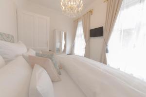 a white bedroom with a large bed and a chandelier at Palais Gutenberg la Ville in Klagenfurt