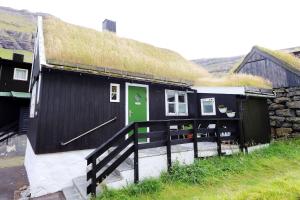 ein schwarzes Haus mit einem Grasdach mit grüner Tür in der Unterkunft holiday cottage in Tjørnuvík in Tjørnuvík