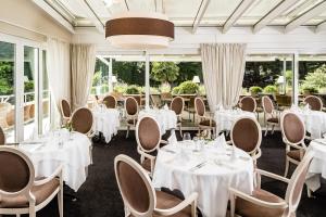 restauracja z białymi stołami, krzesłami i oknami w obiekcie Classic Hotel Meranerhof w Meranie