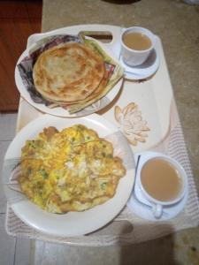 Pearl Cottage Guest House في كراتشي: طاولة مع طبقين من الطعام وكوبين من القهوة