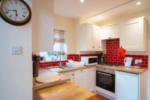 a kitchen with white cabinets and a clock on the wall at The Annexe at Clarendon in Bovey Tracey