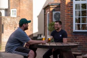 two men sitting on a bench next to a brick building at The Dog & Bear Hotel in Lenham