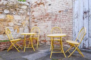 three yellow tables and chairs next to a brick wall at Cromwell Apartment - 3 Red Doors Battery Point in Hobart