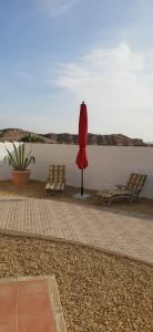 a red umbrella and two chairs next to a wall at Los Torres Casa Lindsay in Arboleas