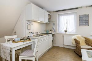 a kitchen with white cabinets and a sink and a table at Strandläufernest in Tinnum