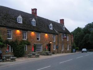 a large brick building with benches in front of it at The George Inn in Lower Brailes