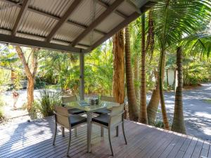 a table and chairs on a deck with palm trees at Mobys Beach house 11 in Boomerang Beach