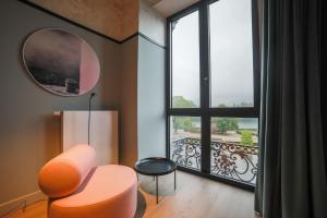 - un salon avec une chaise orange et une grande fenêtre dans l'établissement Hôtel Vedette, à Profondeville