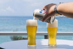 une personne versant de la bière dans deux verres sur une table dans l'établissement ホテル 美らビーチ, à Motobu