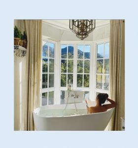 una donna seduta in una vasca da bagno in una stanza con finestre di Luxe Wilderness a Nuwara Eliya