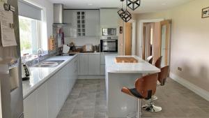a kitchen with white cabinets and a counter with chairs at TÍ Mhaggie Holiday Cottage by Trident Holiday Homes in Gowla