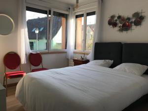 1 dormitorio con 1 cama blanca con 2 sillas y ventanas en le chemin du meunier, en Riquewihr