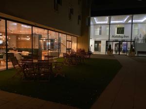 a group of chairs and tables outside a building at night at Holiday Inn Sittingbourne, an IHG Hotel in Sittingbourne