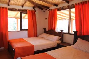 a bedroom with two beds and windows with orange curtains at Posada El Artesano De Raquira in Ráquira
