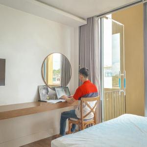 um homem sentado numa secretária com um portátil num quarto de hotel em Cagina Boutique Hostel em Dong Hoi