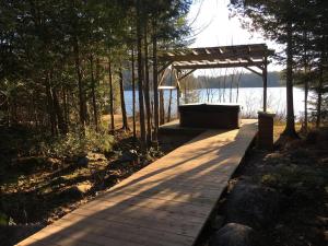 a wooden boardwalk with a pergola next to a lake at Les Chalets du Lac Grenier in Chertsey