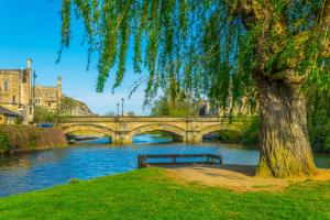 een parkbank onder een boom naast een brug bij Meadow House in Stamford