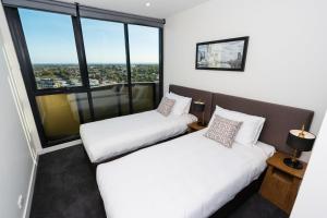 two beds in a room with large windows at The Sebel Melbourne Malvern in Melbourne