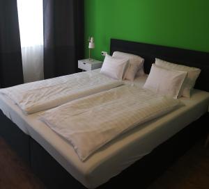 a large bed with white sheets and a green wall at DOMS Gästehaus in Frauenkirchen