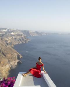une femme en robe rouge assise sur une corniche donnant sur l'océan dans l'établissement Imer Villas, à Imerovigli