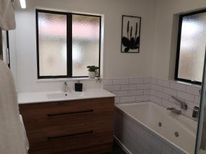 La salle de bains est pourvue d'un lavabo, d'une baignoire et de fenêtres. dans l'établissement Marine Parade Magic - Napier Holiday Home, à Napier
